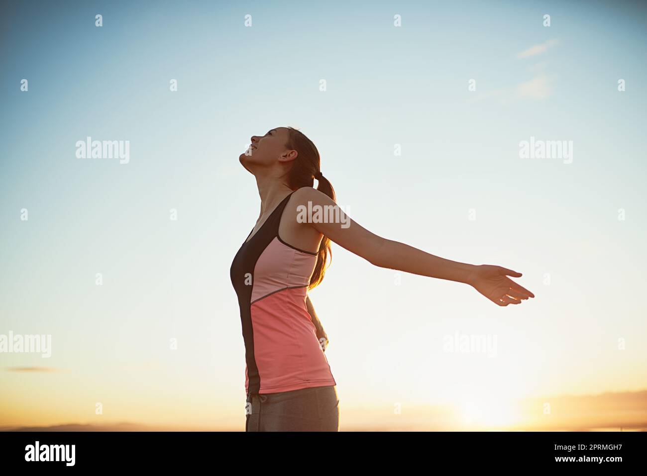 Eine sportliche junge Frau, die mit ausgestreckten Armen im Freien steht. Stockfoto