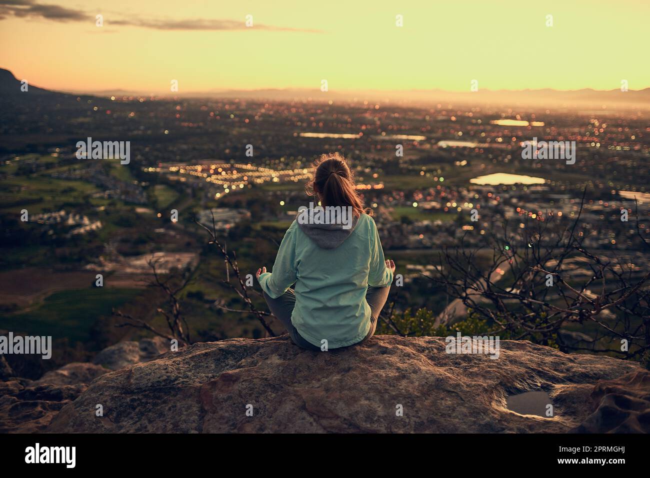 Meditiert an der Spitze. Rückansicht einer sportlichen jungen Frau, die im Freien meditiert. Stockfoto