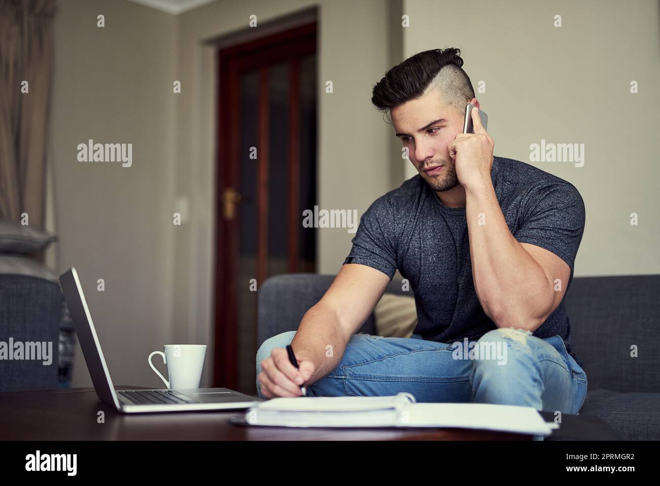 Die Gelegenheit hält nicht die Bürozeiten. Ein fahrender junger Mann nimmt sein Telefon an, während er von seiner Lounge zu Hause aus arbeitet. Stockfoto