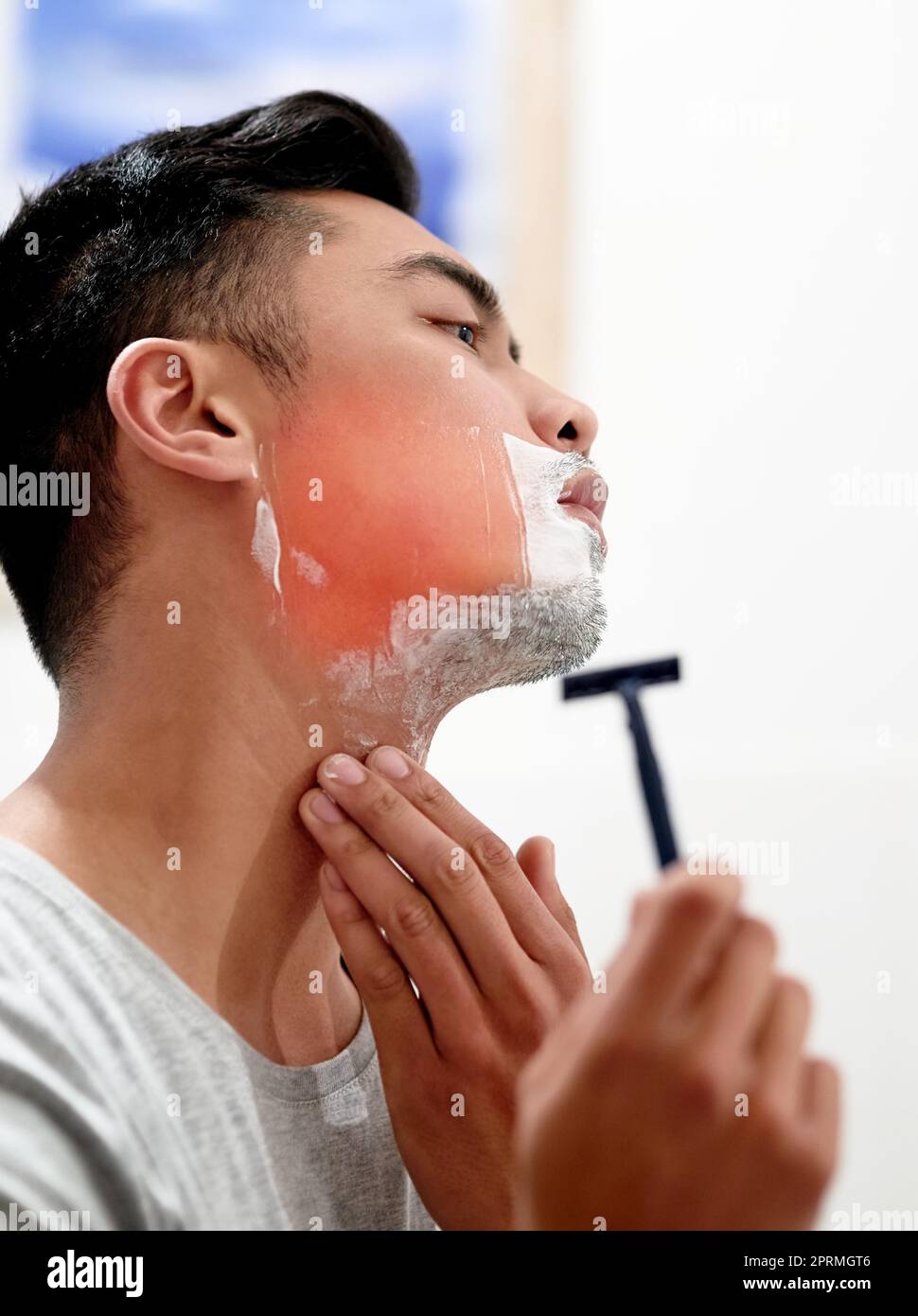 Ein junger Mann zu Hause bekommt von der Rasur mit einem Einwegrasierer einen Rasierbrand im Gesicht. Stockfoto