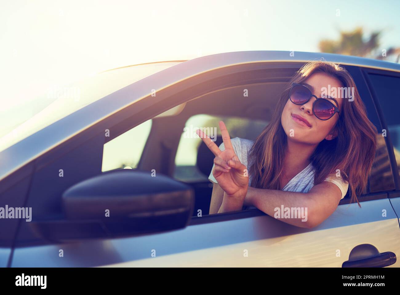 Frieden raus. Porträt einer jungen Frau, die Ihnen das Friedenszeichen gibt, während Sie in ihrem Auto sitzen. Stockfoto