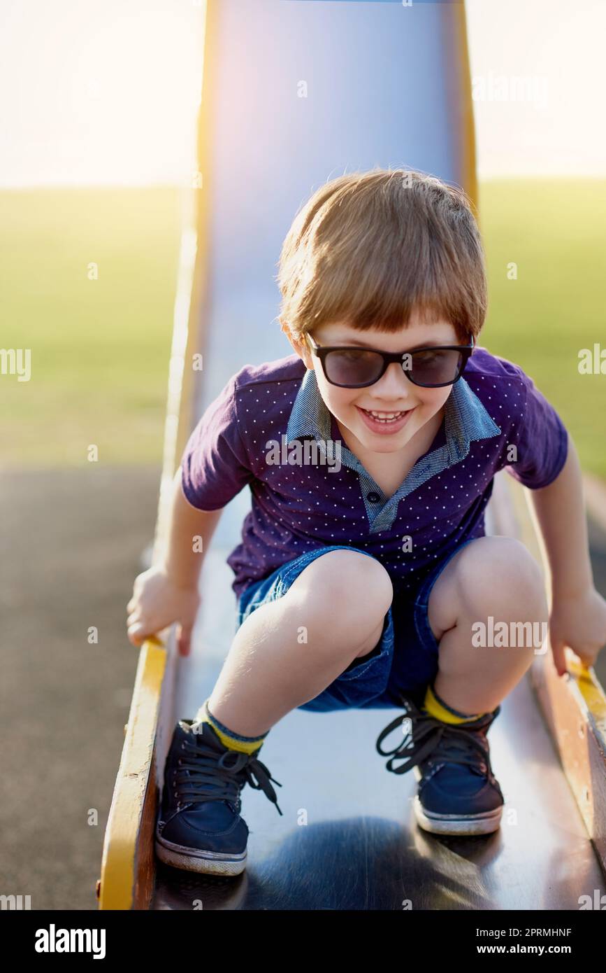 Er kommt gerne auf den Spielplatz. Porträt eines entzückenden kleinen Jungen, der auf einer Rutsche im Park spielt. Stockfoto
