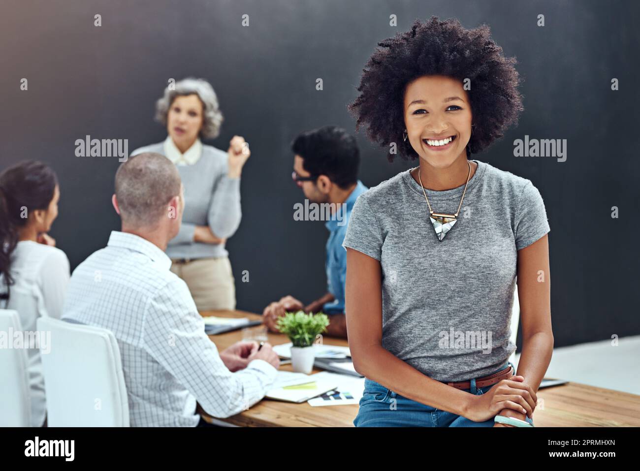 Ich habe meine besten Leute darauf. Porträt einer Geschäftsfrau, die im Sitzungssaal steht, während ein Kollege im Hintergrund eine Präsentation hält. Stockfoto