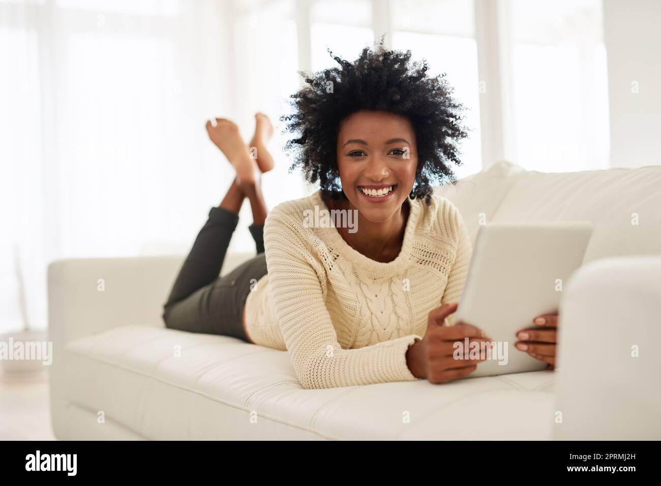 Ich bin ziemlich scharf auf diese Blogging-Sache. Porträt einer attraktiven jungen Person, die ihr Tablet benutzt, während sie zu Hause auf dem Sofa liegt. Stockfoto