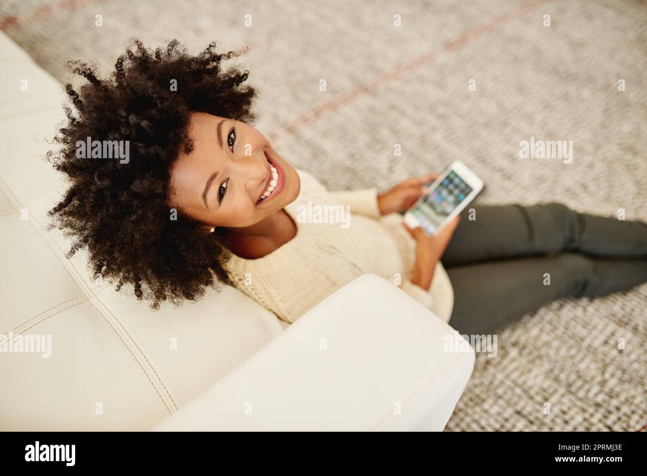 Komfort und Konnektivität. Porträt einer attraktiven jungen Person, die ihr Handy benutzt, während sie zu Hause auf dem Boden sitzt. Stockfoto