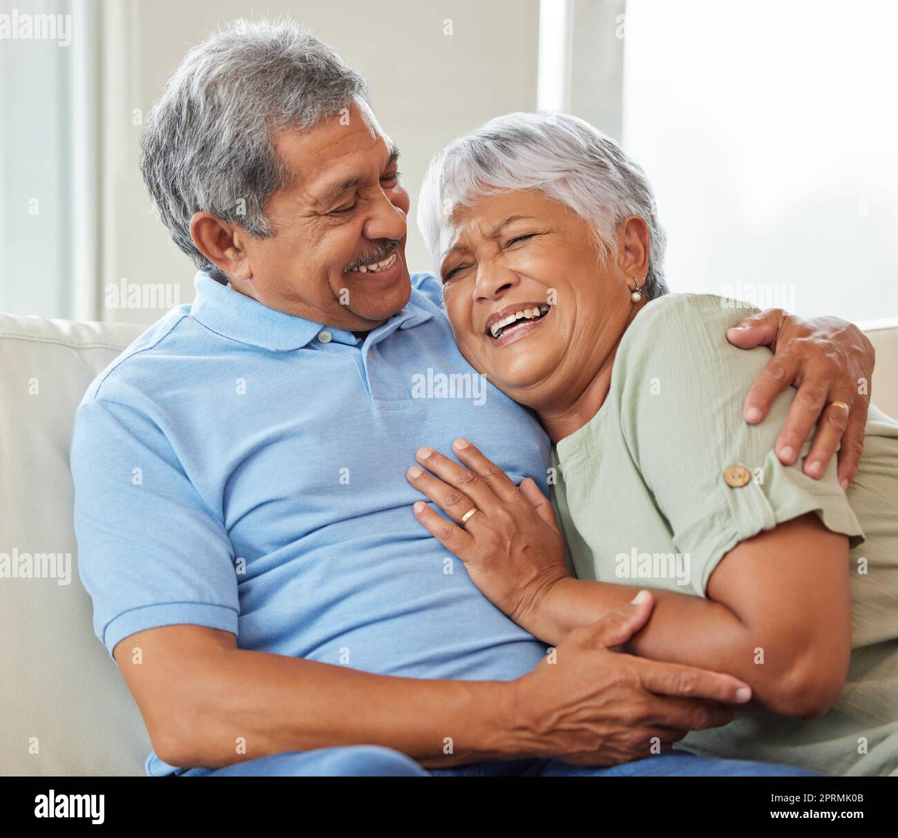 Liebe, Fürsorge und glückliches Seniorenpaar, das sich umarmt, während es sich zu Hause auf dem Sofa verbindet und entspannt. Ältere Männer und Frauen, die auf einer Couch im Wohnzimmer sitzen und umarmen, reden und lachen. Stockfoto
