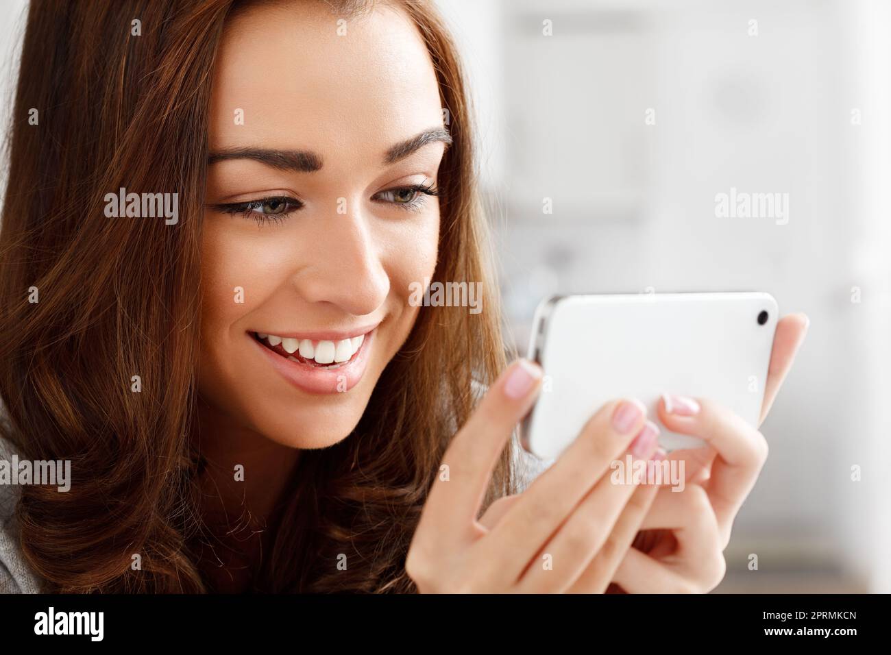 Glückliche Frau, die sich Videos mit einem Telefon ansieht, mit einer Internet-App zum Streamen oder Herunterladen. Junge Dame lächelt, während sie ein lustiges Meme liest oder eine Webserie oder einen Film mit einem Smartphone zu Hause genießt Stockfoto