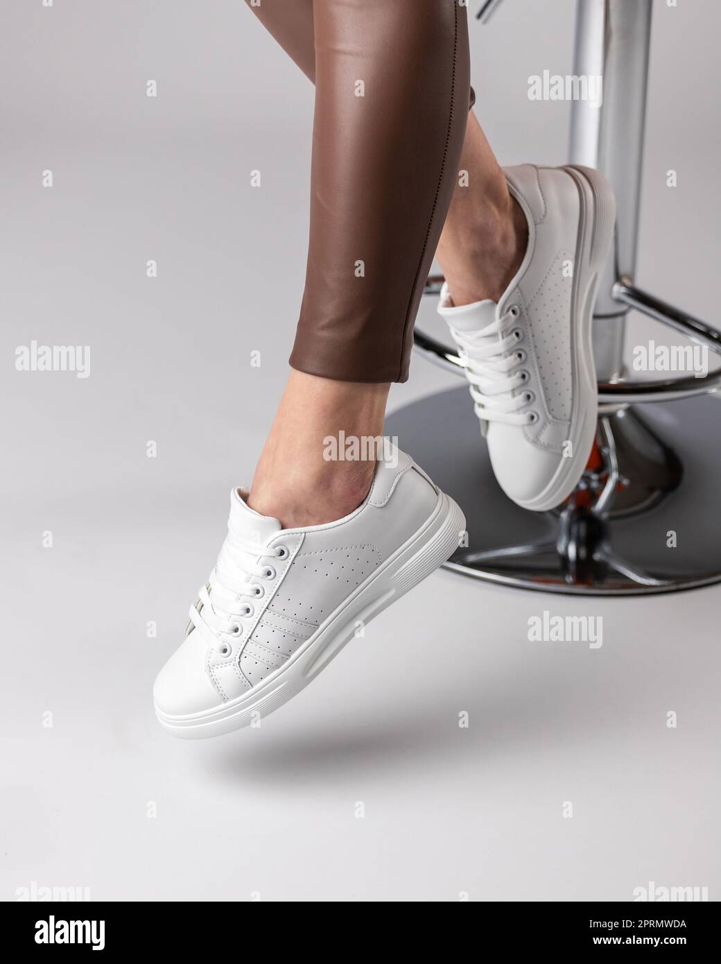 Stylische, moderne Damenschuhe auf den Beinen des Models, die im Studio auf einem Stuhl sitzen und einen weißen Hintergrund haben. Stockfoto