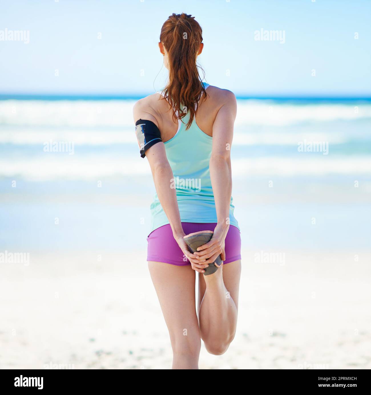 Streckt ihre Muskeln. Rückansicht einer jungen Frau, die sich vor einem Work-out am Strand ausdehnt. Stockfoto