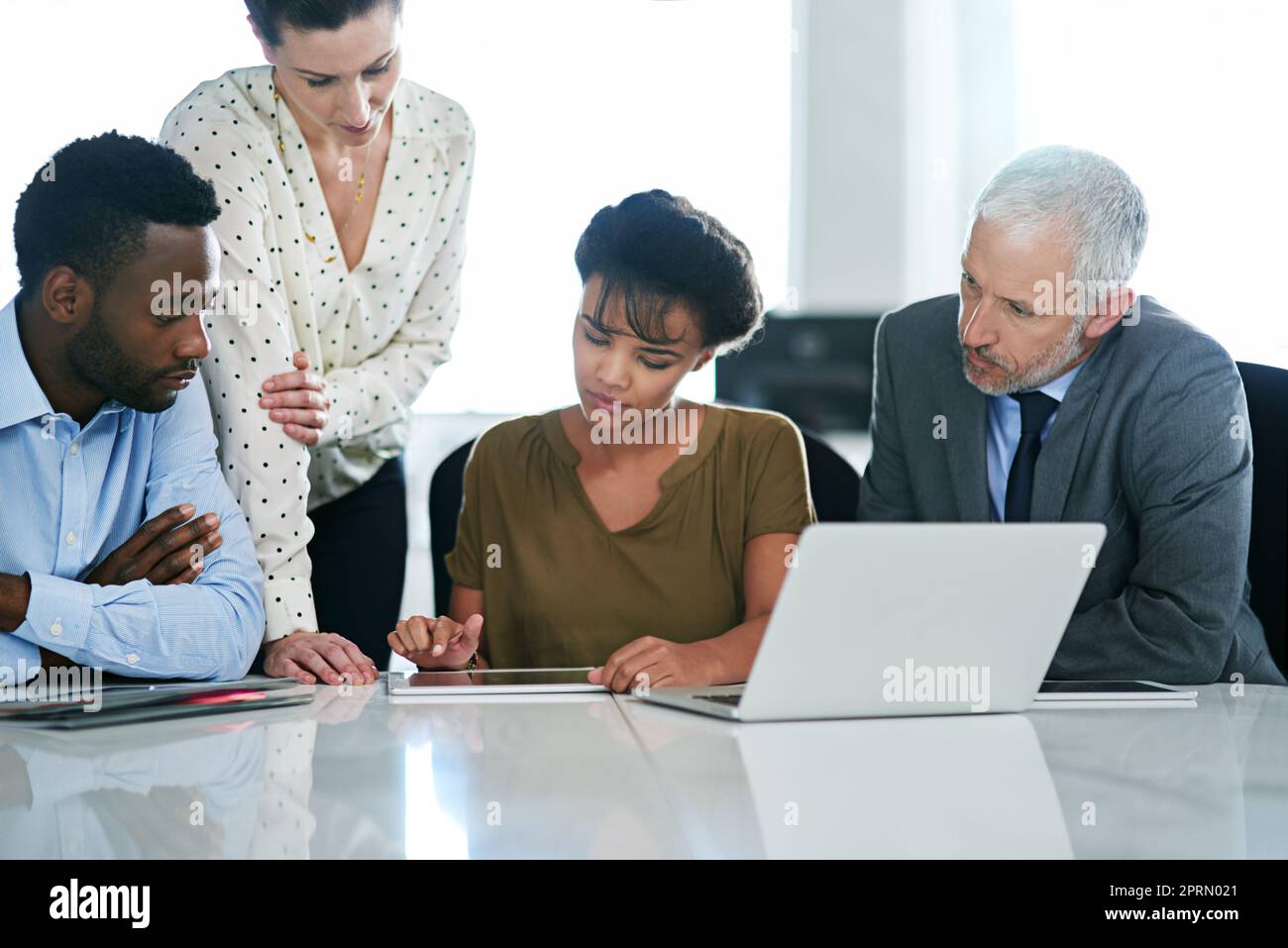 Große Köpfe bei der Arbeit im Büro. Eine Gruppe von Kollegen, die zusammen an einem Laptop arbeiten, während sie an einem Schreibtisch im Büro sitzen. Stockfoto