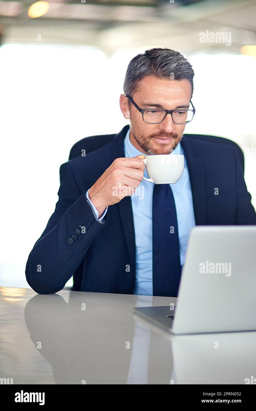 Lesen und Antworten auf seine E-Mails. Ein Geschäftsmann trinkt Kaffee und benutzt einen Laptop im Büro. Stockfoto