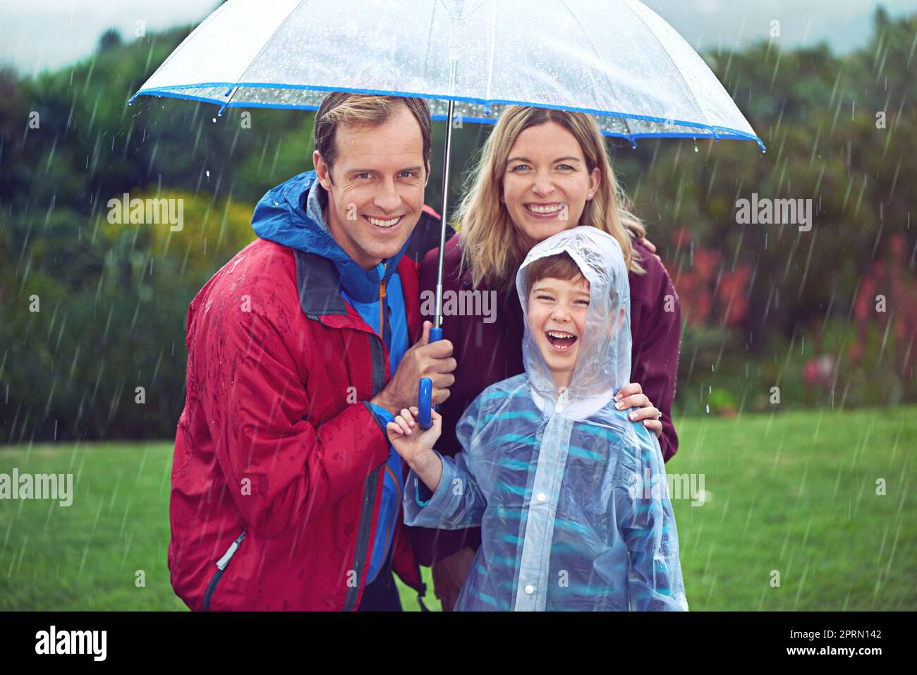 Glück im Regen. Beschnittenes Porträt einer dreiköpfigen Familie, die draußen im Regen steht. Stockfoto