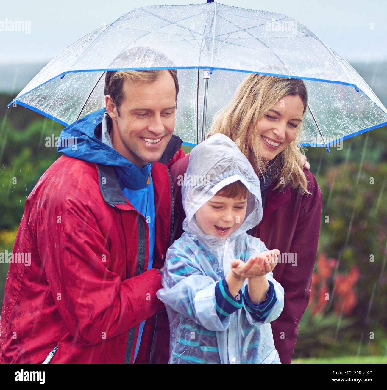 Hes fasziniert vom Regen. Eine dreiköpfige Familie steht draußen im Regen. Stockfoto