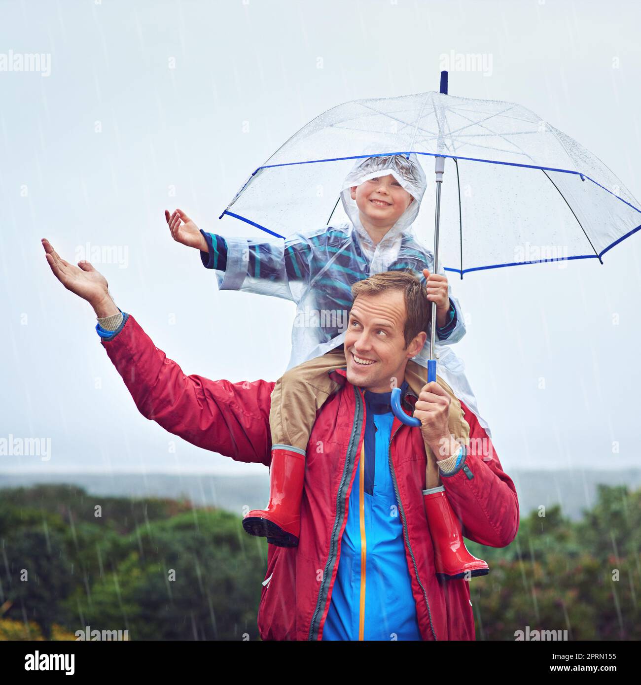 Fangen Sie den Regen. Ein Vater trägt seinen Sohn auf seinen Schultern draußen im Regen. Stockfoto