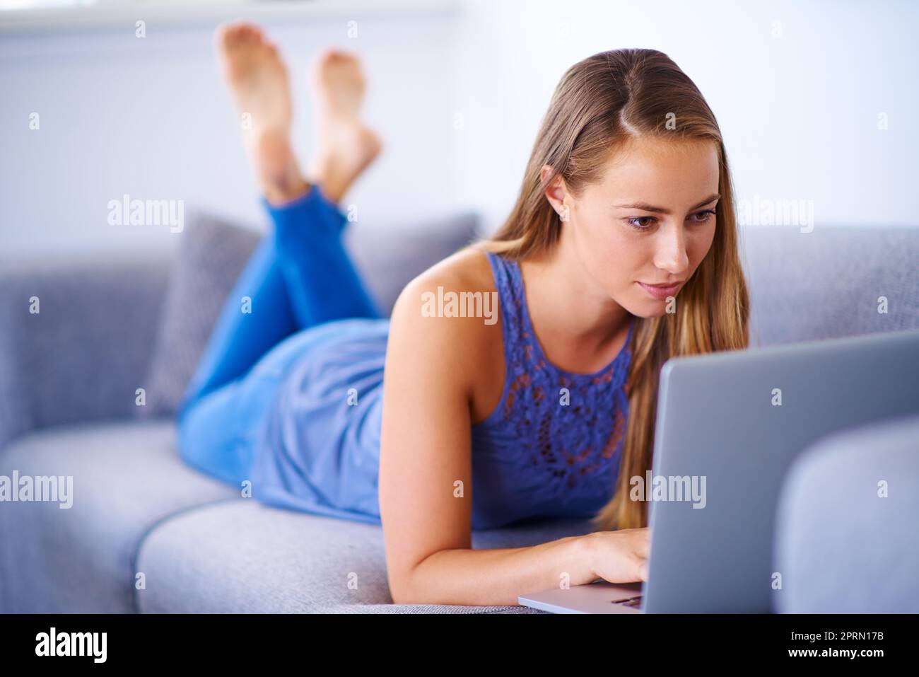Antworten auf einige E-Mails. Eine junge Frau, die ihren Laptop zu Hause auf dem Sofa benutzt. Stockfoto