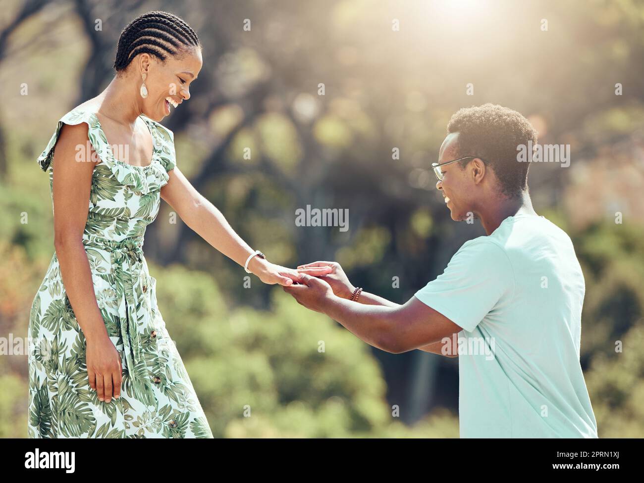 Liebe, Verlobung und schwarzer Mann machen ihrer Freundin einen Heiratsantrag, bei einem romantischen Date draußen, glücklich und aufgeregt. Eine afrikanische Frau überrascht mit einer süßen Geste und genießt einen besonderen Beziehungsmoment bei einem gemeinsamen Date im Freien Stockfoto