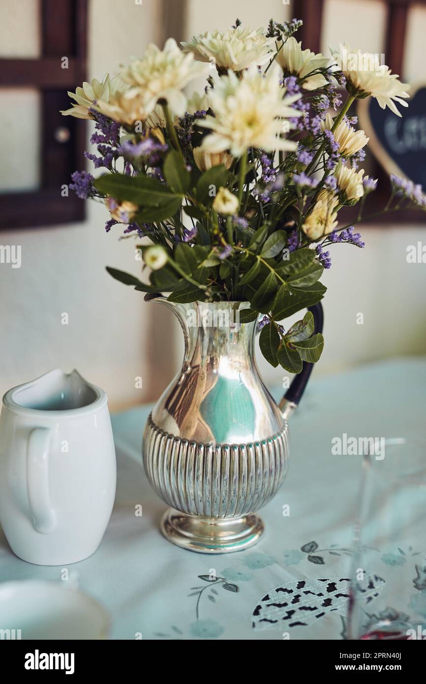 Blumen runden die Tischeinstellungen perfekt ab. Eine Metallvase gefüllt mit Blumen auf einem Tisch bei einer Teeparty drinnen Stockfoto