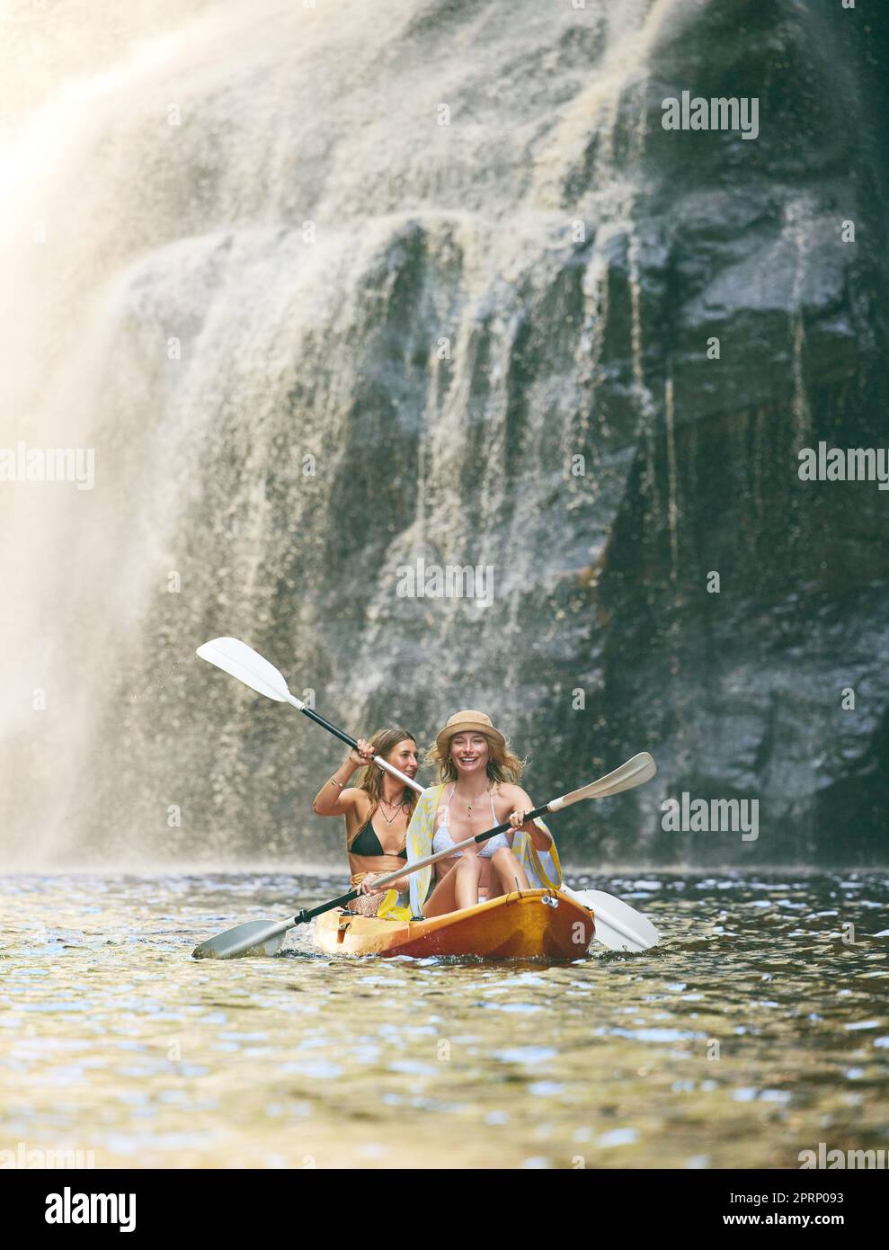 Kajak, Sommer und Freunde auf dem Fluss, Natur und Urlaubsabenteuer zusammen in Bikini-Badeanzug. Urlaub, Wasserfall und Freiheit mit jungen, glücklichen Frauen, die in einer Kanufahrtour mit dem Boot rudern Stockfoto