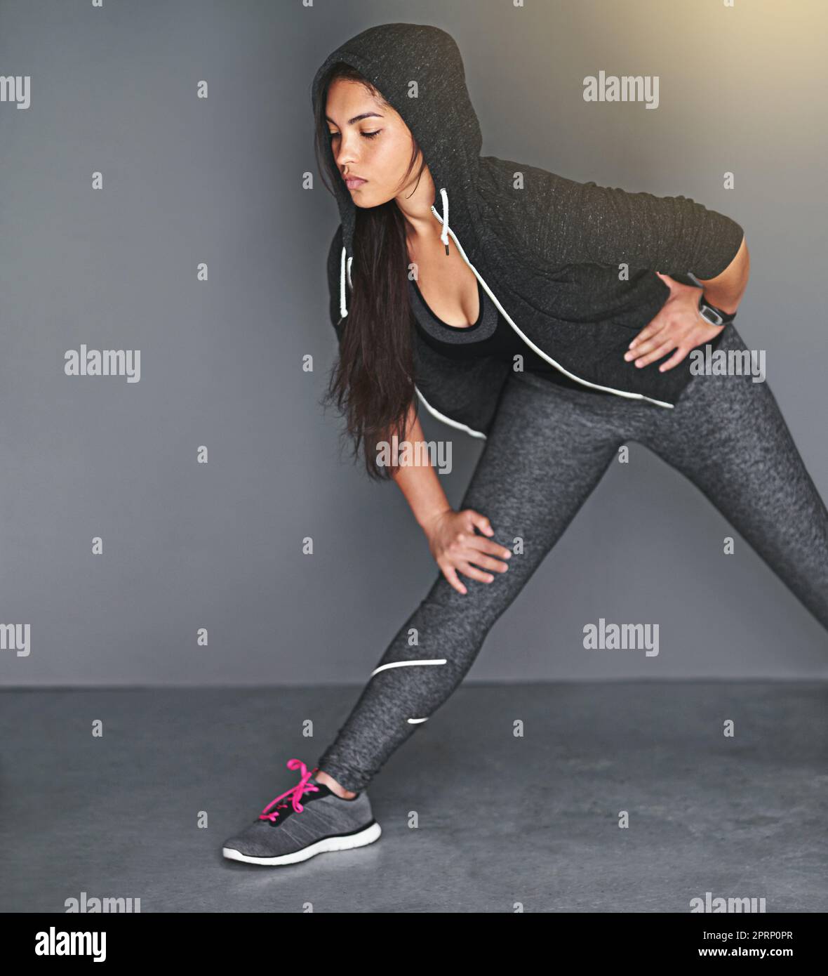 Streckt ihre Beinmuskeln aus. Eine fit junge Frau streckt ihre Beine vor einem grauen Hintergrund. Stockfoto