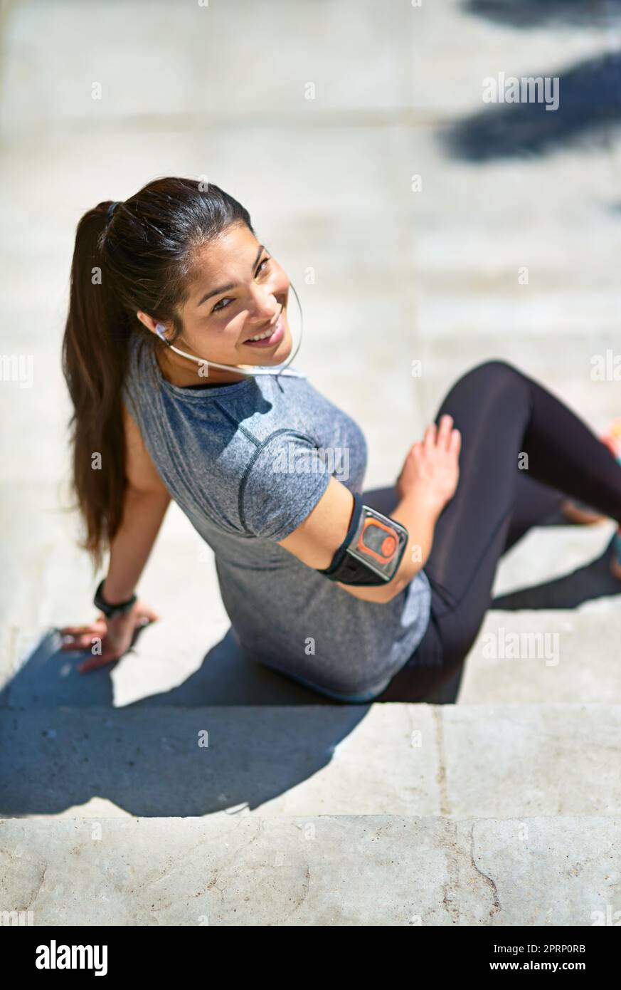 Motiviert, fit zu werden. Eine sportliche junge Frau, die Musik hört, während sie draußen auf Treppen sitzt. Stockfoto