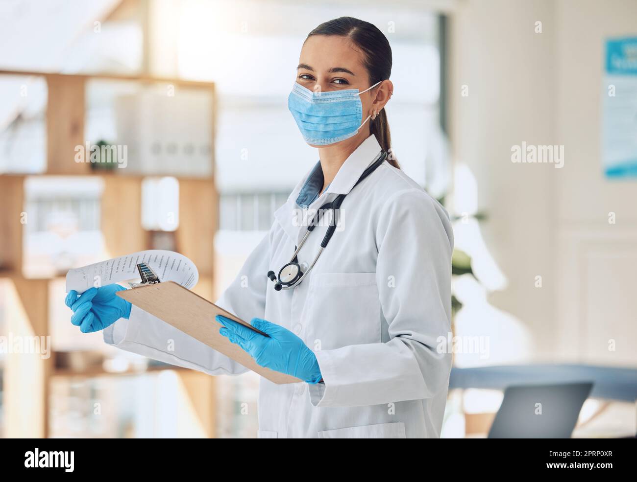 Porträt eines Arztes mit Papier und Gesichtsmaske, der während der Covid-Pandemie medizinische Papiere macht. Gesundheitspersonal liest Coronavirus-Ergebnisse auf einem Clipboard von Krankenhauspatienten im Stehen in der Klinik. Stockfoto