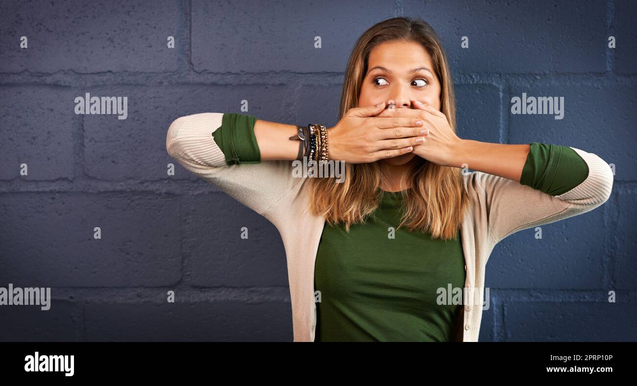 Oh nein, Ive hat zu viel gesagt... eine junge Frau, die ihren Mund vor einem Backsteinmauer-Hintergrund bedeckte. Stockfoto