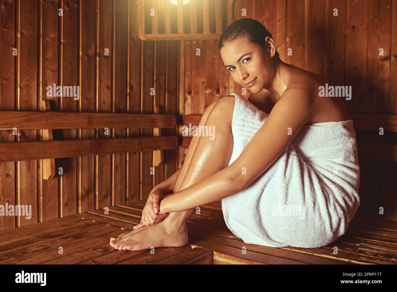 Diese Sauna fühlt sich toll an. Ganzkörperportrait einer jungen Frau, die sich in der Sauna in einem Spa entspannt. Stockfoto