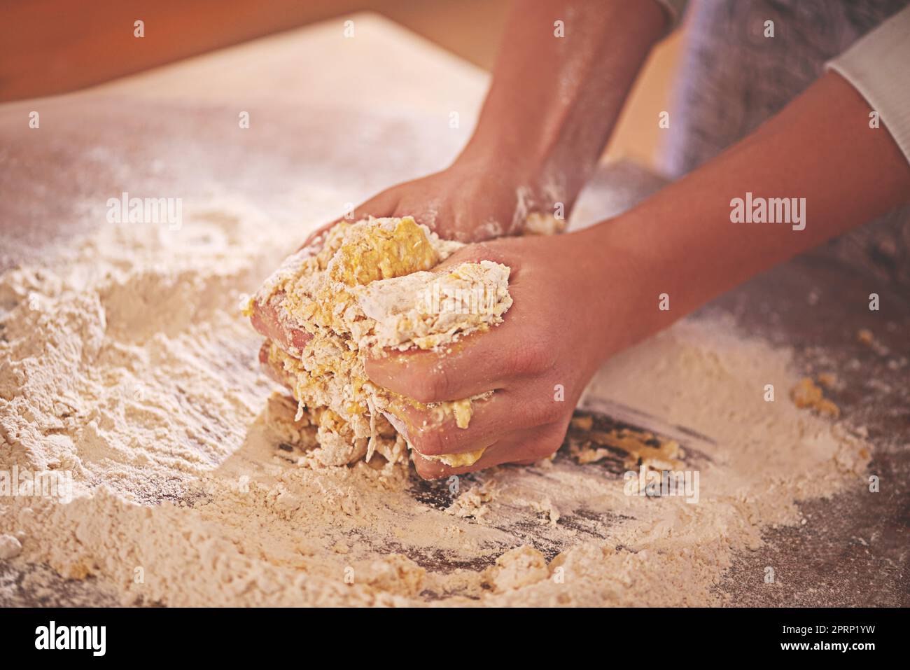 Die Kunst der Herstellung von Pasta. Eine Person, die Nudelteig auf einer bemehlten Tischplatte knetet. Stockfoto