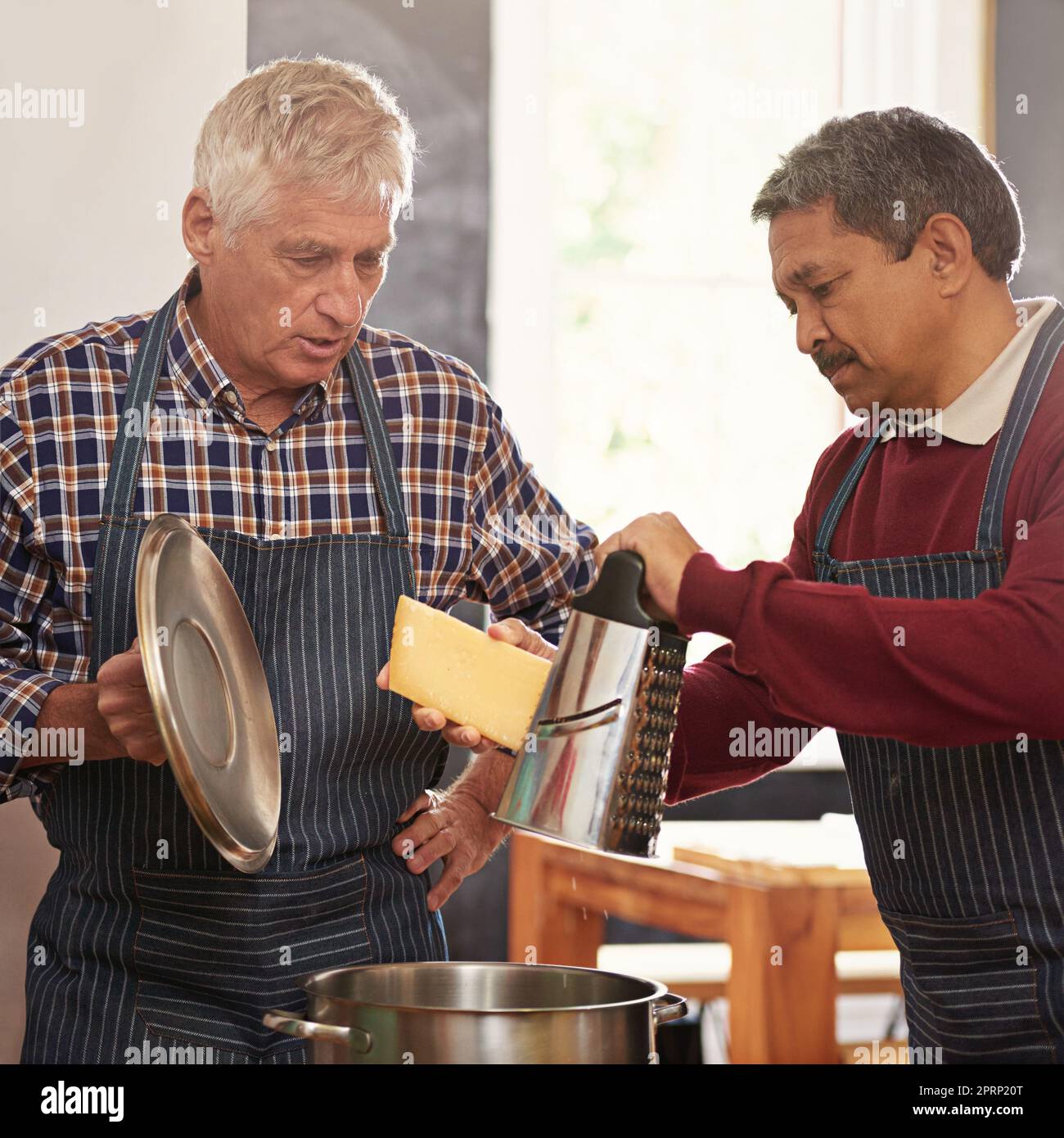 Es geht um den Käse. Zwei ältere Männer kochen in der Küche. Stockfoto