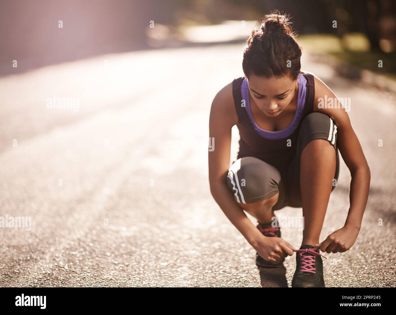 Der einzige Weg zum Ziel ist der Start. Eine Läuferin bindet ihre Schnürsenkel vor einem Lauf. Stockfoto