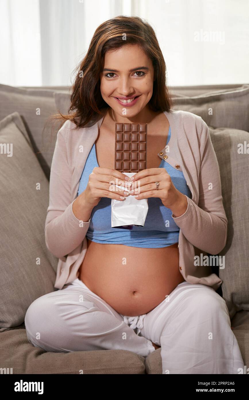 Wenn das Verlangen eingreift. Eine junge Schwangere, die zu Hause eine Schokoladenplatte isst. Stockfoto