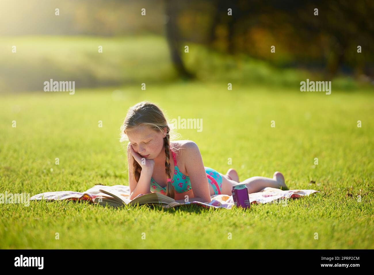 Ihr Sommer ist ausgebucht. Ein Teenager-Mädchen, das sich mit einem Buch auf dem Rasen entspannt. Stockfoto