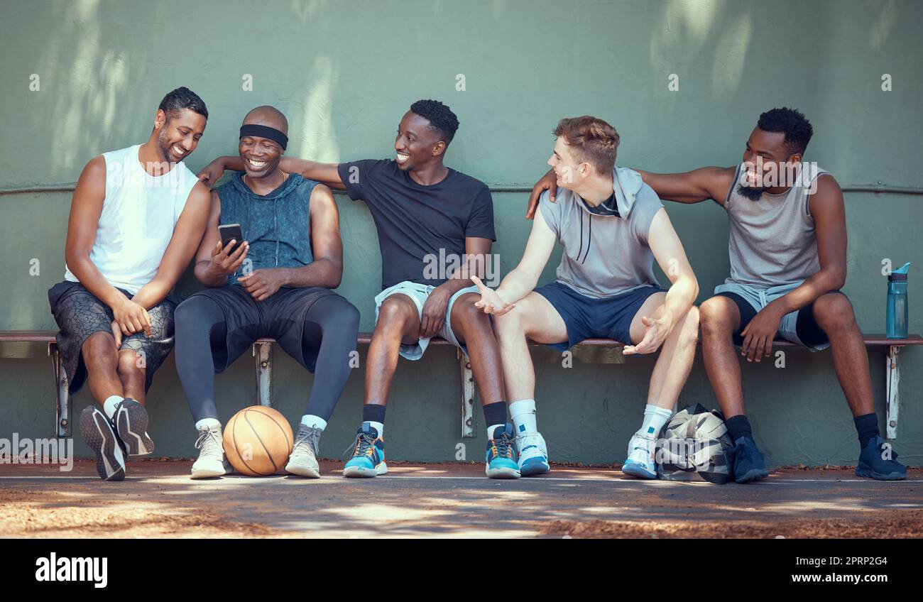 Basketball, Sport und Freunde mit einem Team von Männern, die nach Training, Training oder einem Spiel auf einer Bank sitzen. Teamwork, Telefon und Training mit einer Gruppe von Baseballspielern draußen auf einem Sportplatz Stockfoto