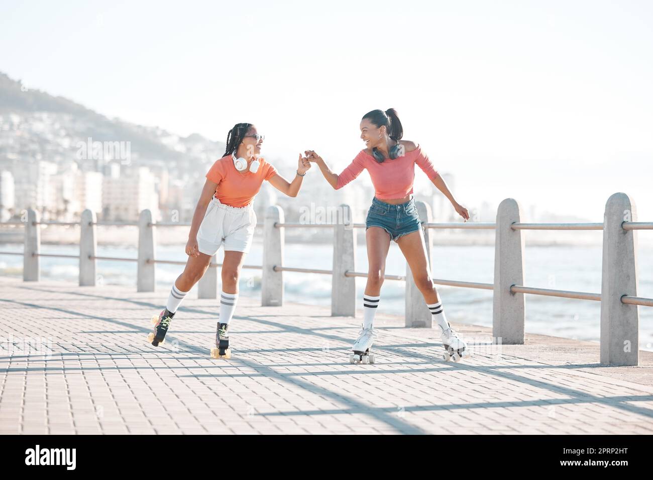 Schwarze Frauen, Faust- und Rollschuhfahrer, fröhliche Freunde am Meer, am Meer oder an der Küste. Unterstützung, Partnerschaft und Zusammenarbeit von Mädchen oder Spaß auf gemeinsamen Promenadenfahrten. Stockfoto