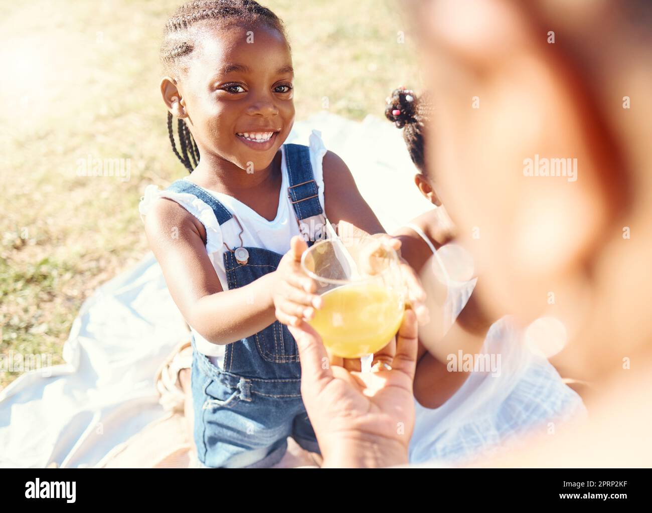 Glückliches Mädchen, Saft und Lächeln in der Familie Picknick Spaß und Freude in Glück an einem warmen Sommertag in der Natur. Schwarzes Kind lächelt für frisches kaltes, gesundes Getränk im Freien mit Eltern und Geschwistern Stockfoto