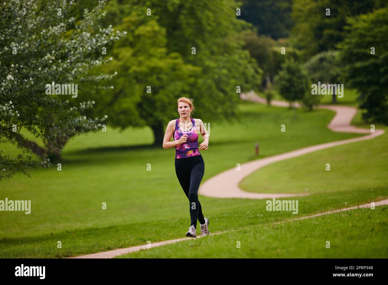 Sie liebt ein einsames Joggen. Eine Frau, die in einem Park entlang eines Fußwegs joggt. Stockfoto