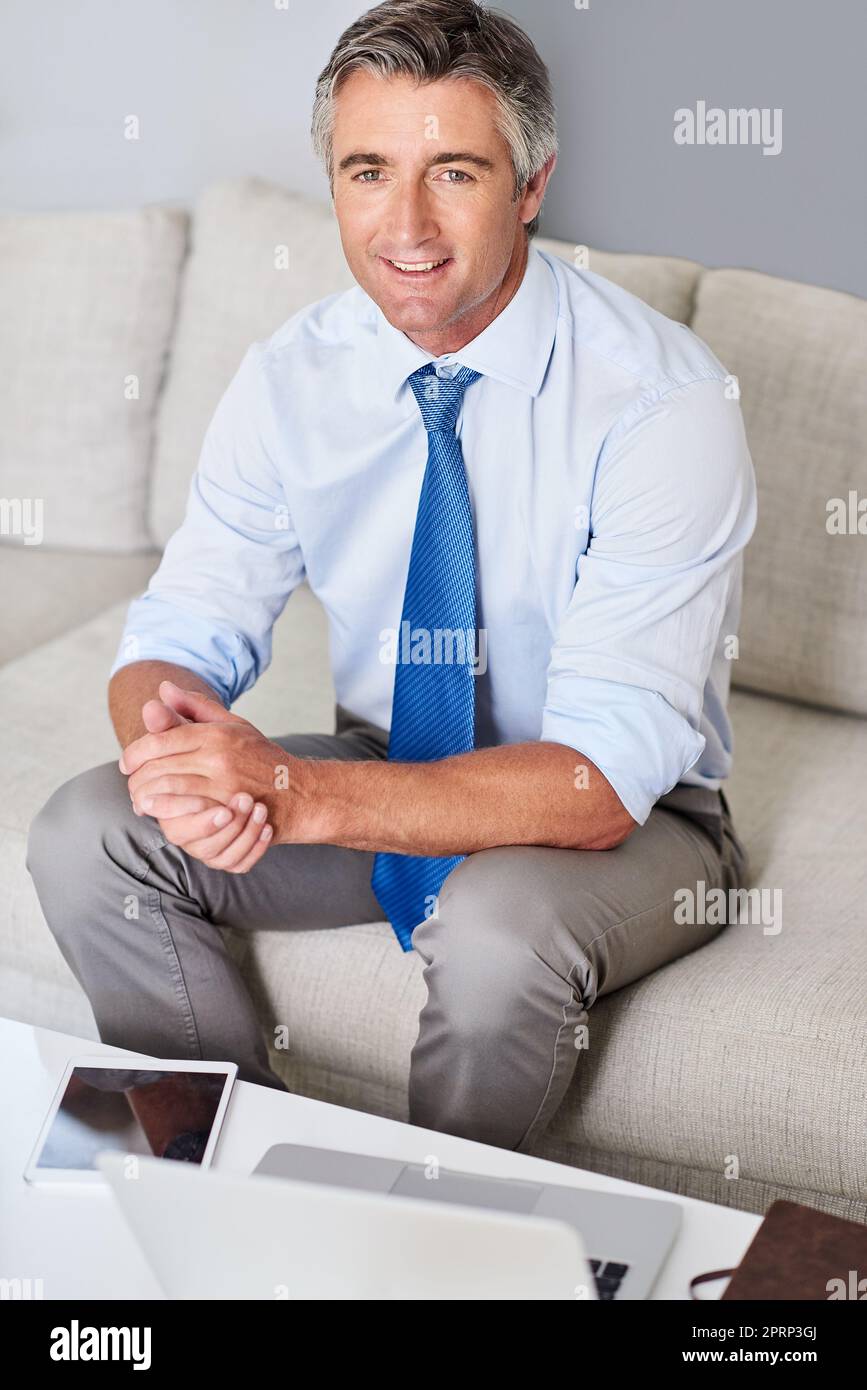 So sieht Erfolg aus. Porträt eines reifen Geschäftsmannes, der lächelt und mit den Händen auf einem Sofa sitzt. Stockfoto