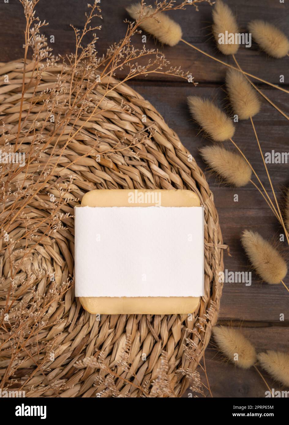 Seifenleiste mit leerem Etikett auf einem gezackten Tischset in der Nähe von Hare's Tail Gras. Kosmetisches Modell Stockfoto