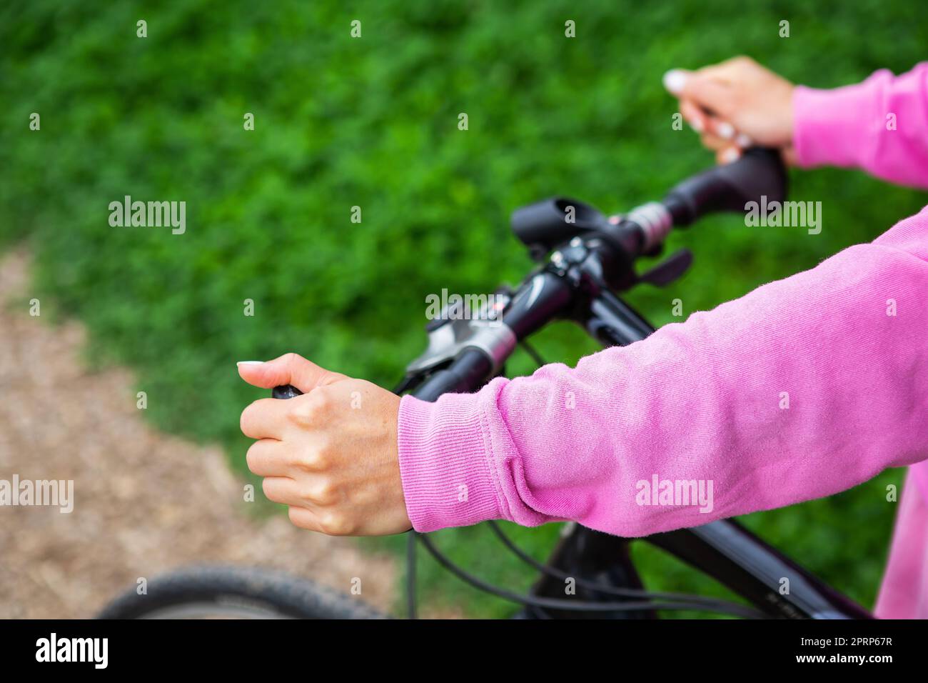 Ein Mädchen in einem rosa Sweatshirt hält sich am Lenker eines Fahrrads fest, eine Fahrradtour im Park. Erholung im Freien ist gut für die Gesundheit. Stockfoto