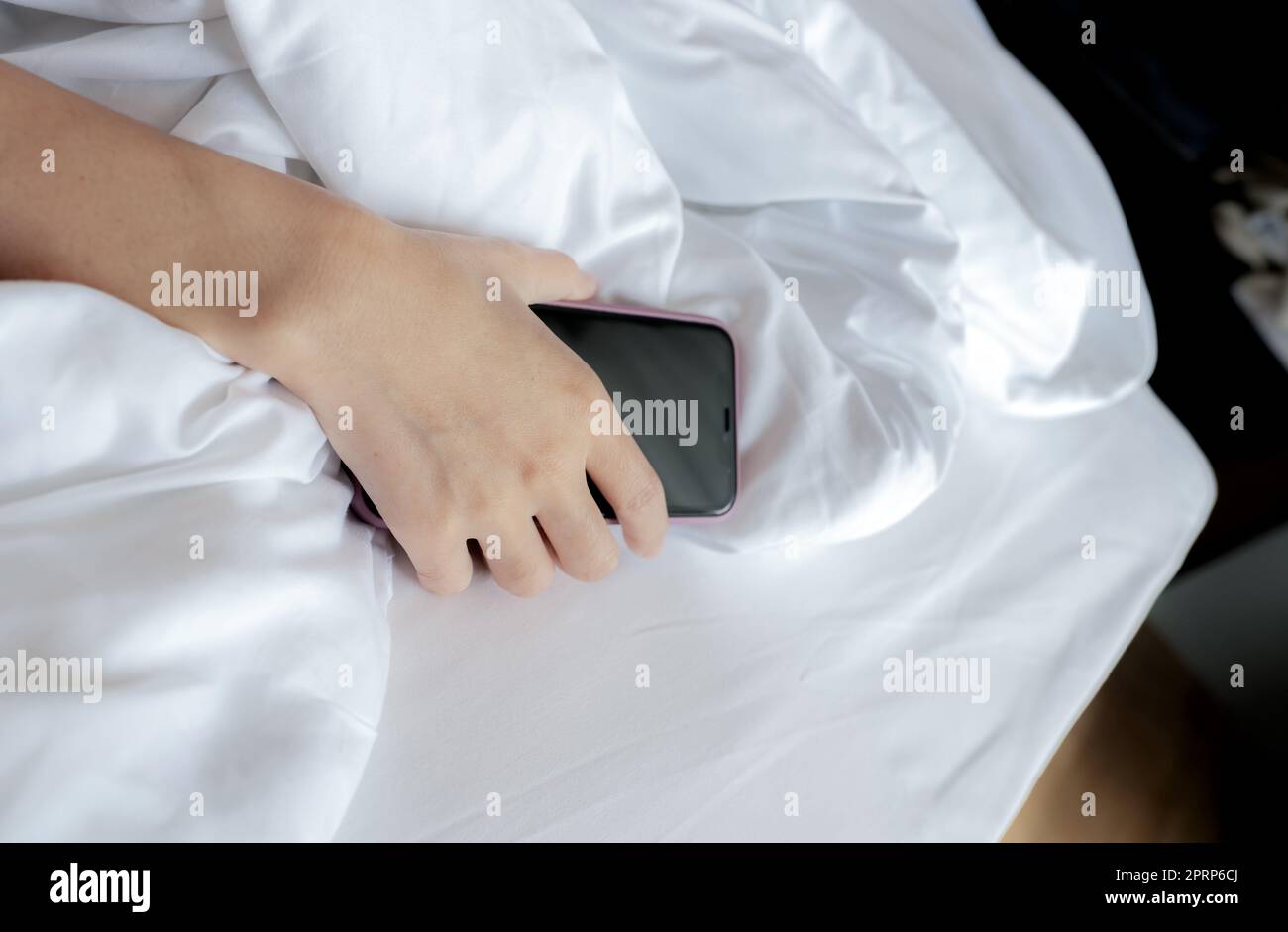 Frau schläft im Bett und Hand hält Handy. Frau, die im Schlafzimmer ein Smartphone benutzt. Eine Frau, die Smartphone benutzt. SMS auf dem Handy mit Müdigkeit bis zum Einschlafen. Sie schläft mit dem Smartphone. Stockfoto