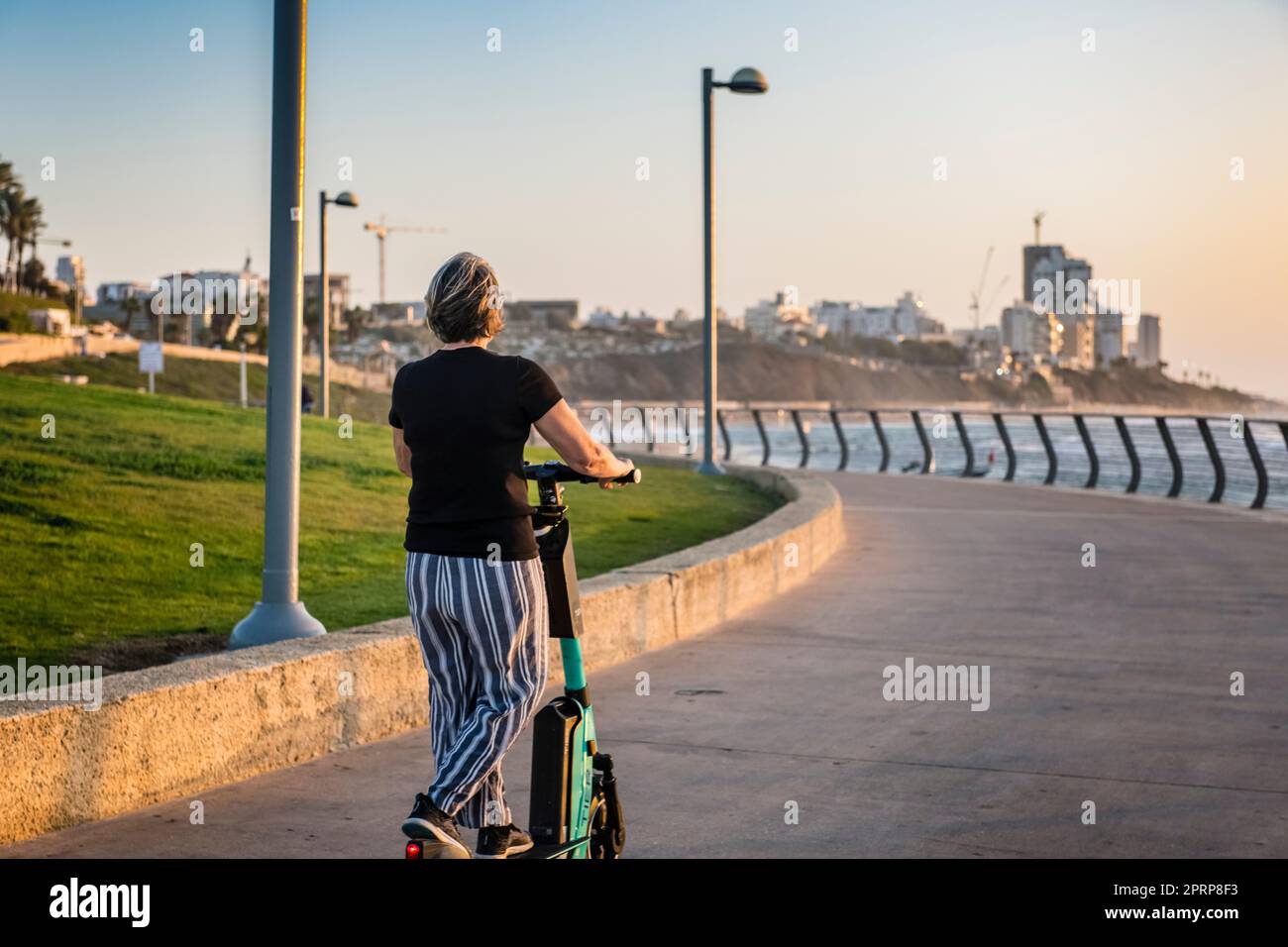 Aktiv jung im Herzen 60s Frau/Frau, die einen Elektroroller auf der Promenade in Tel Aviv Israel benutzt Stockfoto