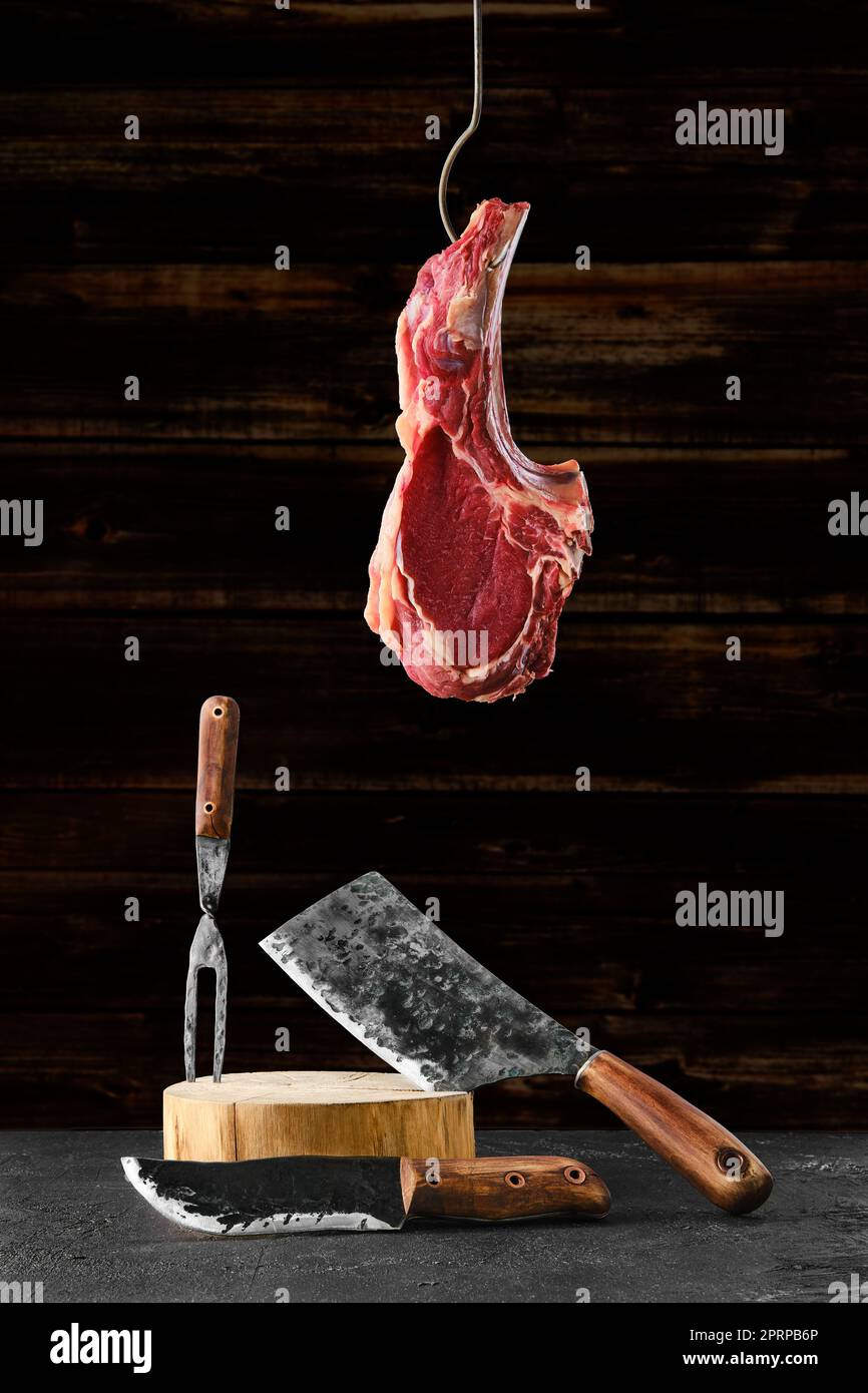 Rind Ribeye Steak Knochen-in auf Stahlhaken über dem geschmiedeten Metzger-Set Stockfoto