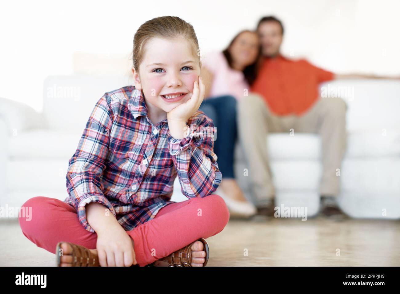 Was für ein hübsches Lächeln. Ein kleines Mädchen posiert mit ihren Eltern im Hintergrund. Stockfoto