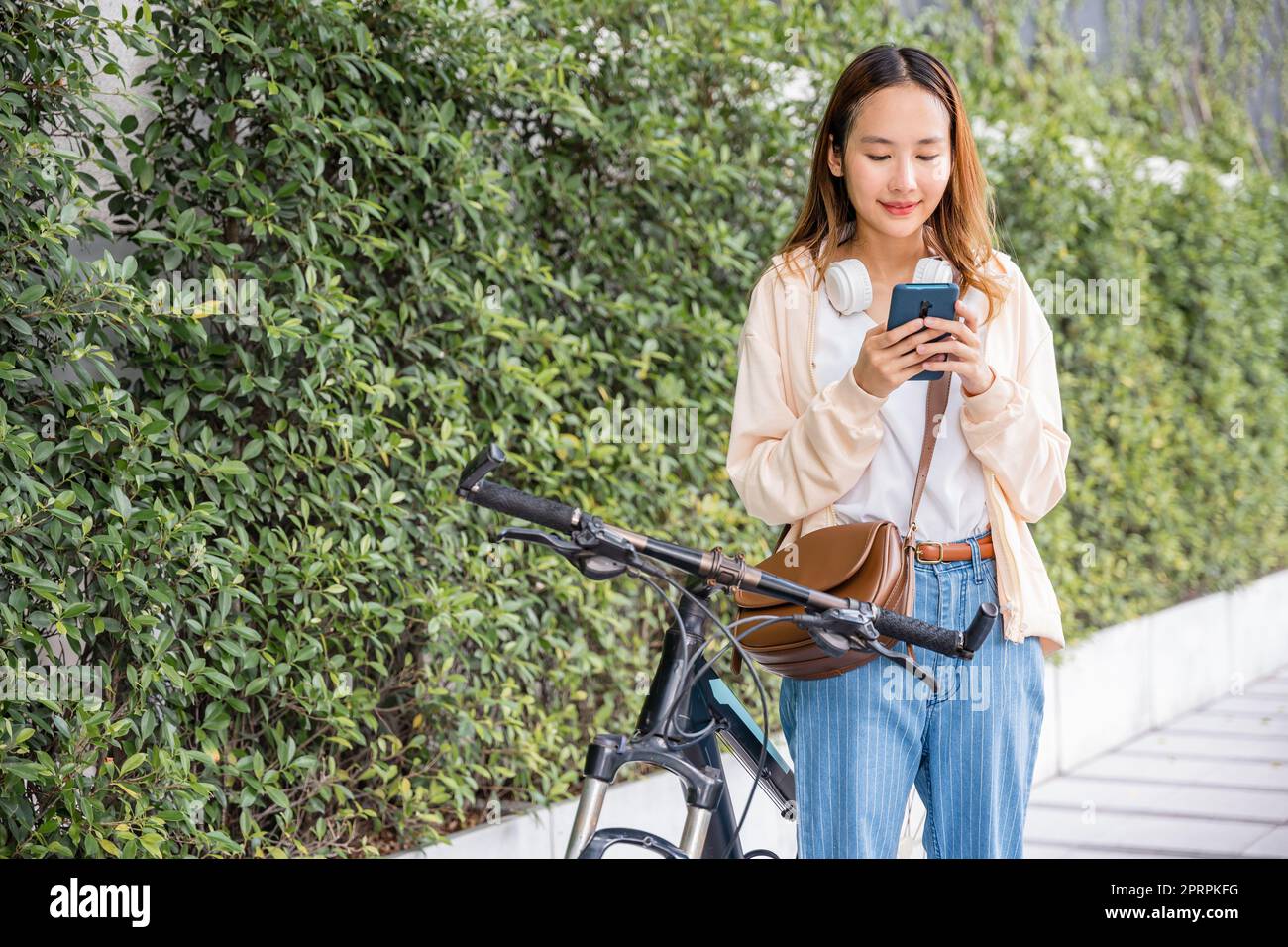 Frau pendelt im Sommer mit dem Fahrrad auf dem Smartphone in Parklandschaft Stockfoto