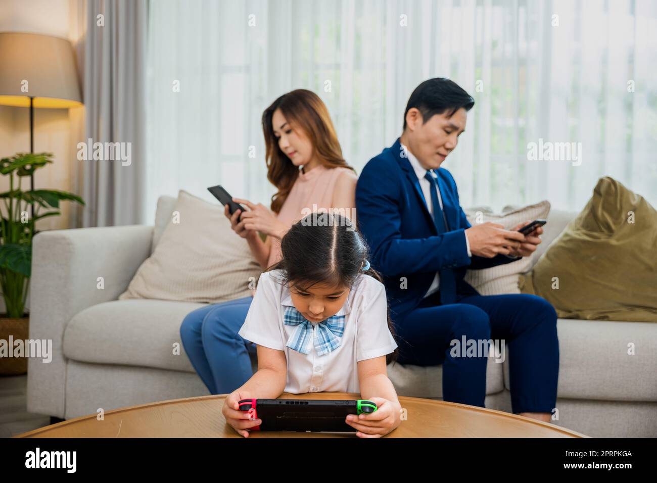 Asiatische Eltern ignorieren ihr Kind und schauen zu Hause auf ihr Handy Stockfoto