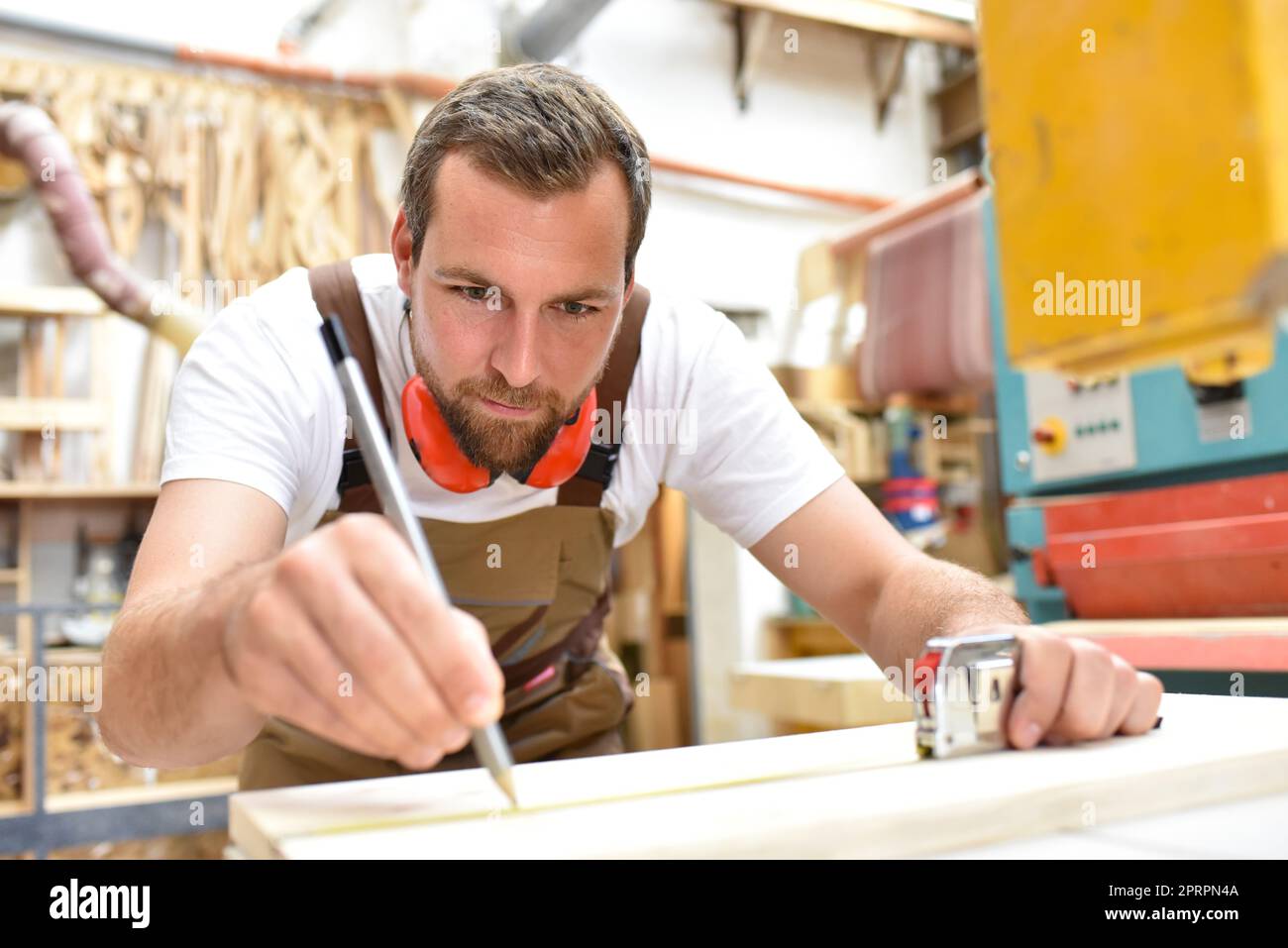 Freundlich Tischler mit Gehörschutz und Arbeitskleidung arbeiten an einer Säge in der Werkstatt Stockfoto