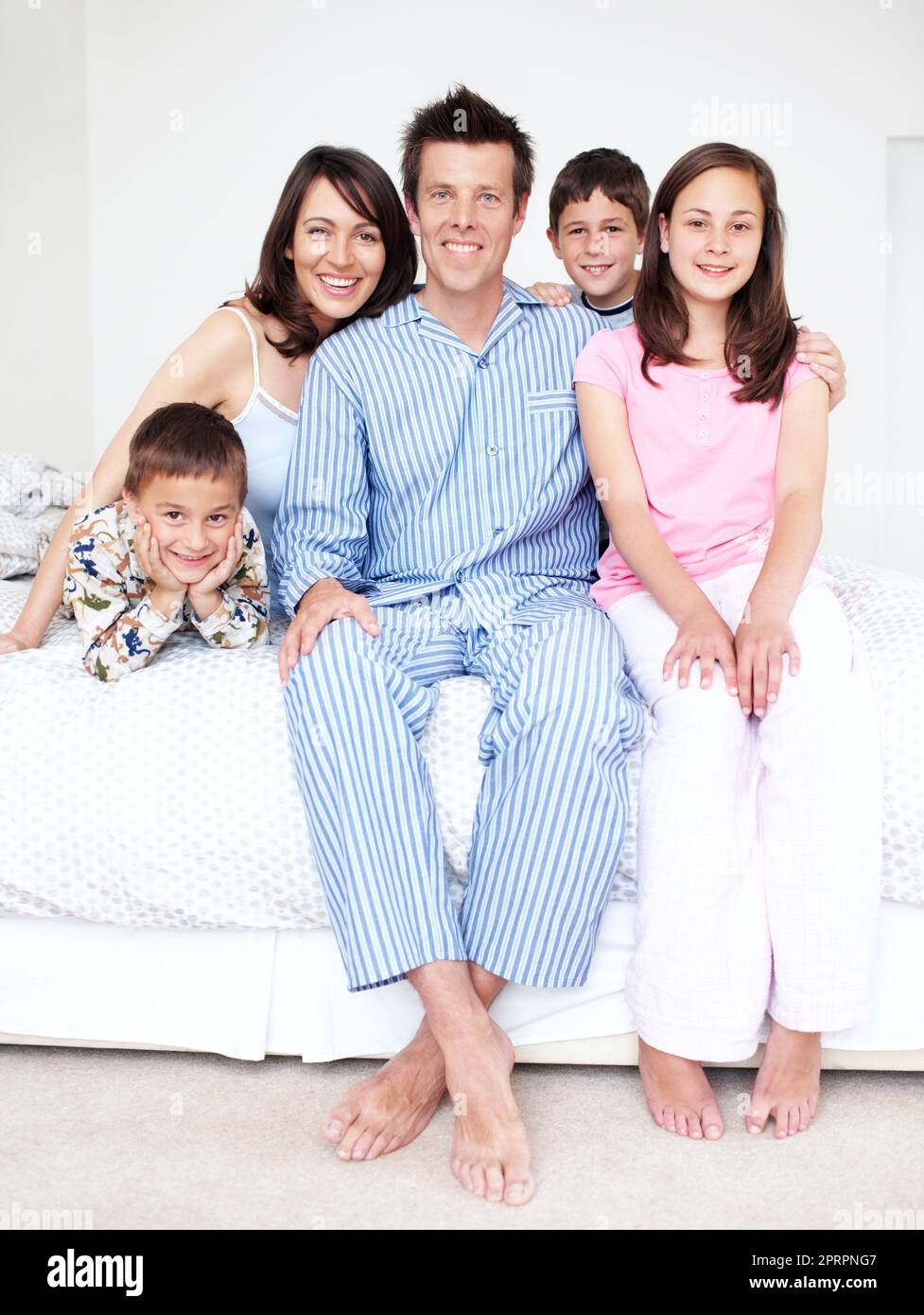 Er hätte nicht stolzer auf seine Familie sein können. Eine liebevolle fünfköpfige Familie, die in ihrem Schlafanzug auf einem Bett sitzt. Stockfoto
