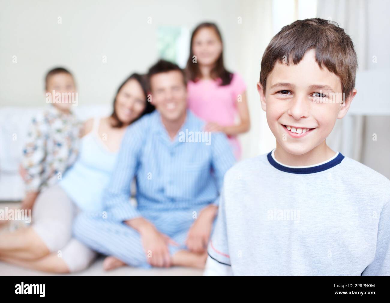 Eine glänzende Zukunft vor ihm. Porträt eines niedlichen kleinen Jungen lächelt glücklich, während seine Familie sitzt unscharf im Hintergrund - Copyspace. Stockfoto