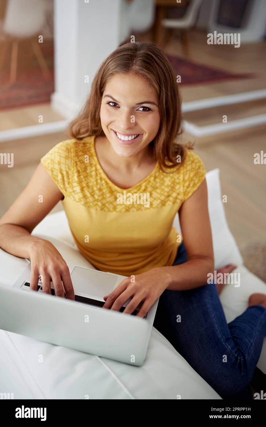 Warten Sie nur, bis Sie meinen neuesten Artikel sehen. Das verkürzte Porträt einer attraktiven jungen Frau, die einen Laptop benutzt, während sie zu Hause auf einem Sofa sitzt. Stockfoto