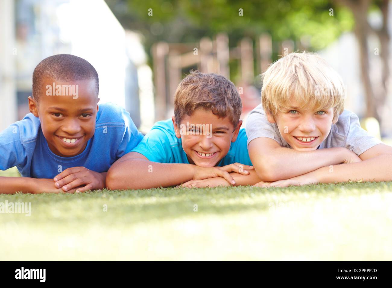 Pausenzeit-Freunde. Porträt von drei niedlichen Jungen, die an einem sonnigen Nachmittag auf dem Gras liegen - Copyspace. Stockfoto